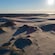 A sand dune stretches towards a large body of water on the horizon as the sun sets